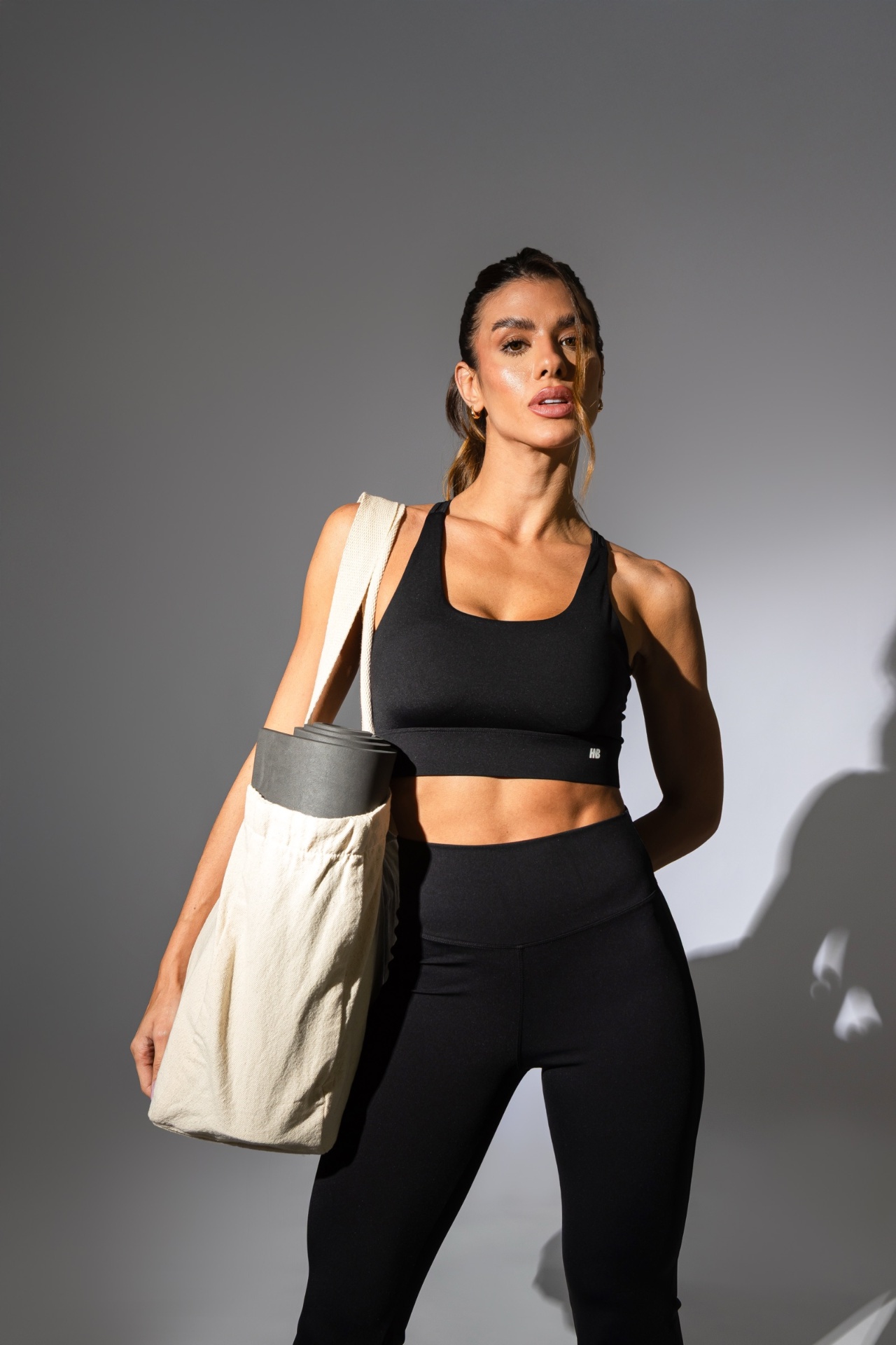 Modelo Honey Be com top e legging pretos, iluminação editorial em estúdio cinza